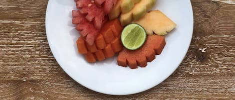 A white plate with various fruits including watermelon, cantaloupe, and lime on a wooden surface.
