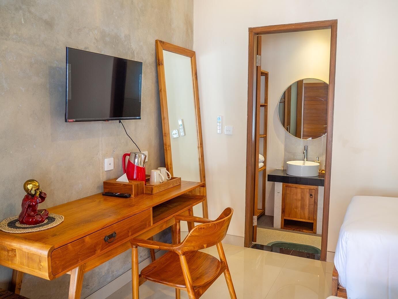 Habitación de hotel con escritorio de madera, televisor montado en la pared, un espejo grande, baño con lavamanos y espejo, y una cama.