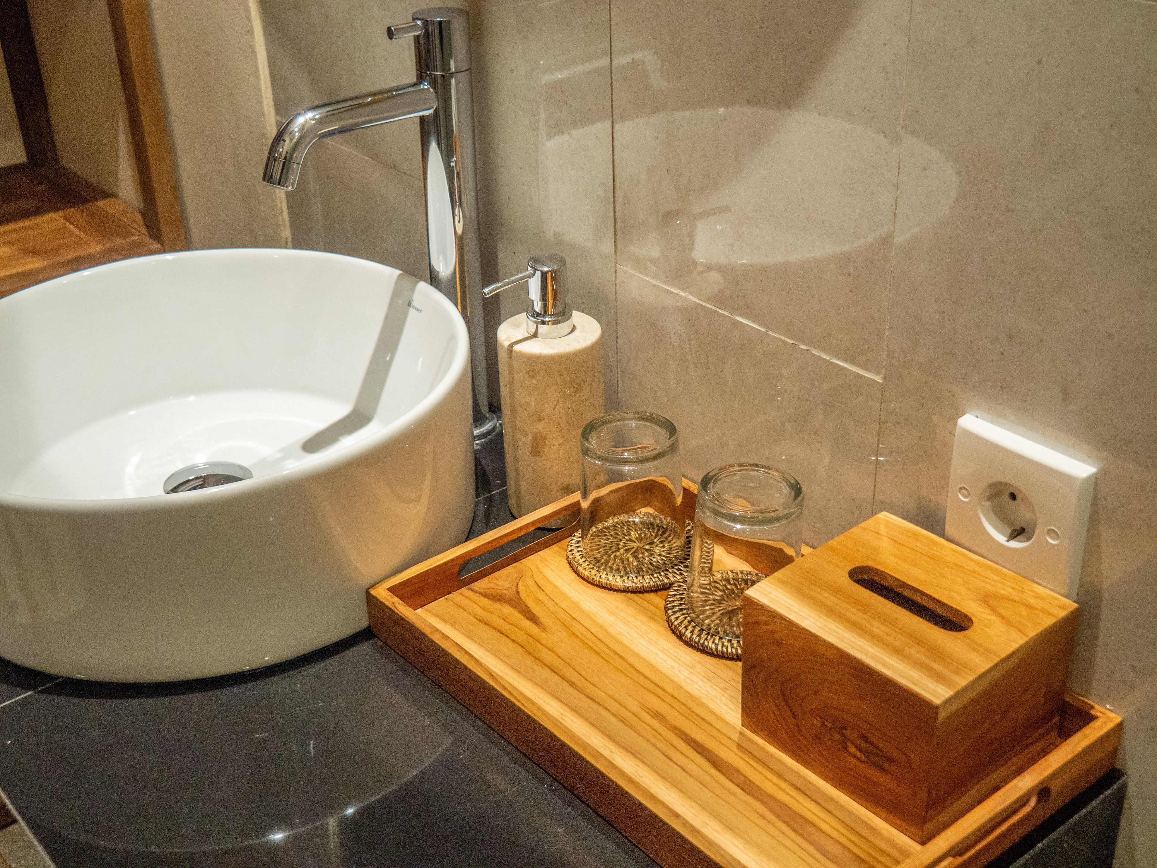 A bathroom with a white sink, a wooden tray with decorative items, and a towel rack.