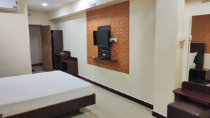 A hotel room with a bed, a TV mounted on a textured wall, a desk, and a wardrobe. - Annai Residency (Mayiladuthurai)