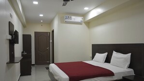 A hotel room with a bed, a TV, a desk, and an air conditioning unit. - Annai Residency (Mayiladuthurai)