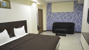 A hotel room with a bed, a sofa, a TV, and a wall with a geometric pattern. - Annai Residency (Mayiladuthurai)