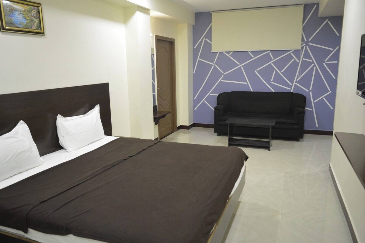 Una habitación de hotel con cama, sofá, televisión y una pared con diseño geométrico.