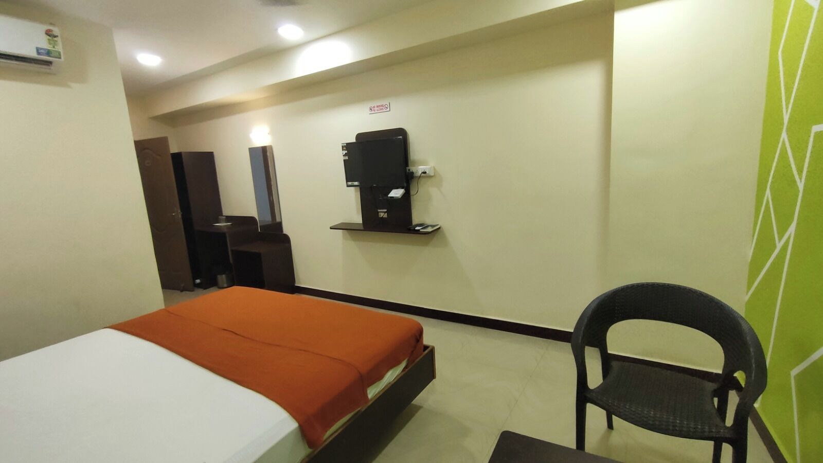 A hotel room with a bed, a chair, a desk, and a wall-mounted coffee machine.