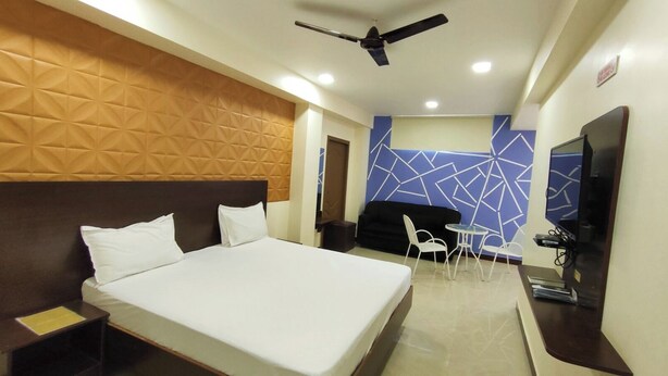 A hotel room with a large bed, a desk with a chair, a small table with chairs, a TV, and a ceiling fan. - Annai Residency (Mayiladuthurai)