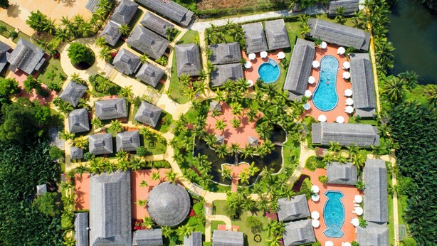 Vue aérienne d’un complexe hôtelier comprenant plusieurs hébergements de type bungalow, un espace piscine central et une végétation luxuriante environnante.