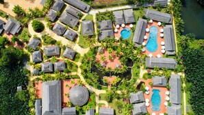 Vue aérienne d’un complexe hôtelier comprenant plusieurs hébergements de type bungalow, un espace piscine central et une végétation luxuriante environnante.
