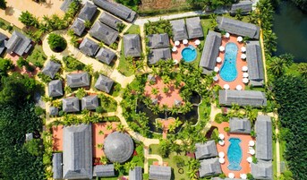 Vista aérea de un complejo turístico con varias cabañas, un área de piscina central y follaje circundante.
