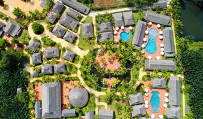 Eine Vogelperspektive zeigt ein Resort mit mehreren Bungalows, einem zentralen Poolbereich und dichter Vegetation.