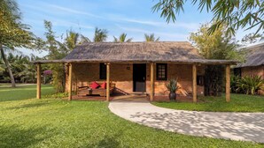 A single-story building with a thatched roof, a covered porch, and a seating area with a bench and cushions. - ENSO Retreat Hoi An - Rediscovery & Serenity (Da Nang)