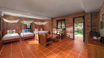 Una camera d'albergo con parete in mattoni, pavimento piastrellato e un'ampia finestra. Si vedono due letti, un tavolo e una sedia.