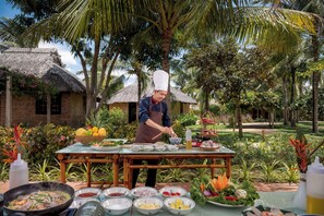 Een kok bereidt eten buiten, met een tafel vol ingrediënten en keukengerei.