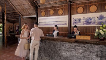 A reception desk with a sign reading 'RECEPTION', a receptionist, and a couple standing in front of it.