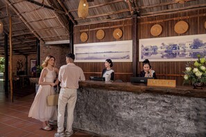 A reception desk with a sign reading 'RECEPTION', a receptionist, and a couple standing in front of it.