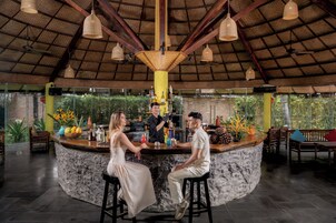 Uma área de bar com balcão de pedra, cadeiras de madeira e luminárias pendentes.