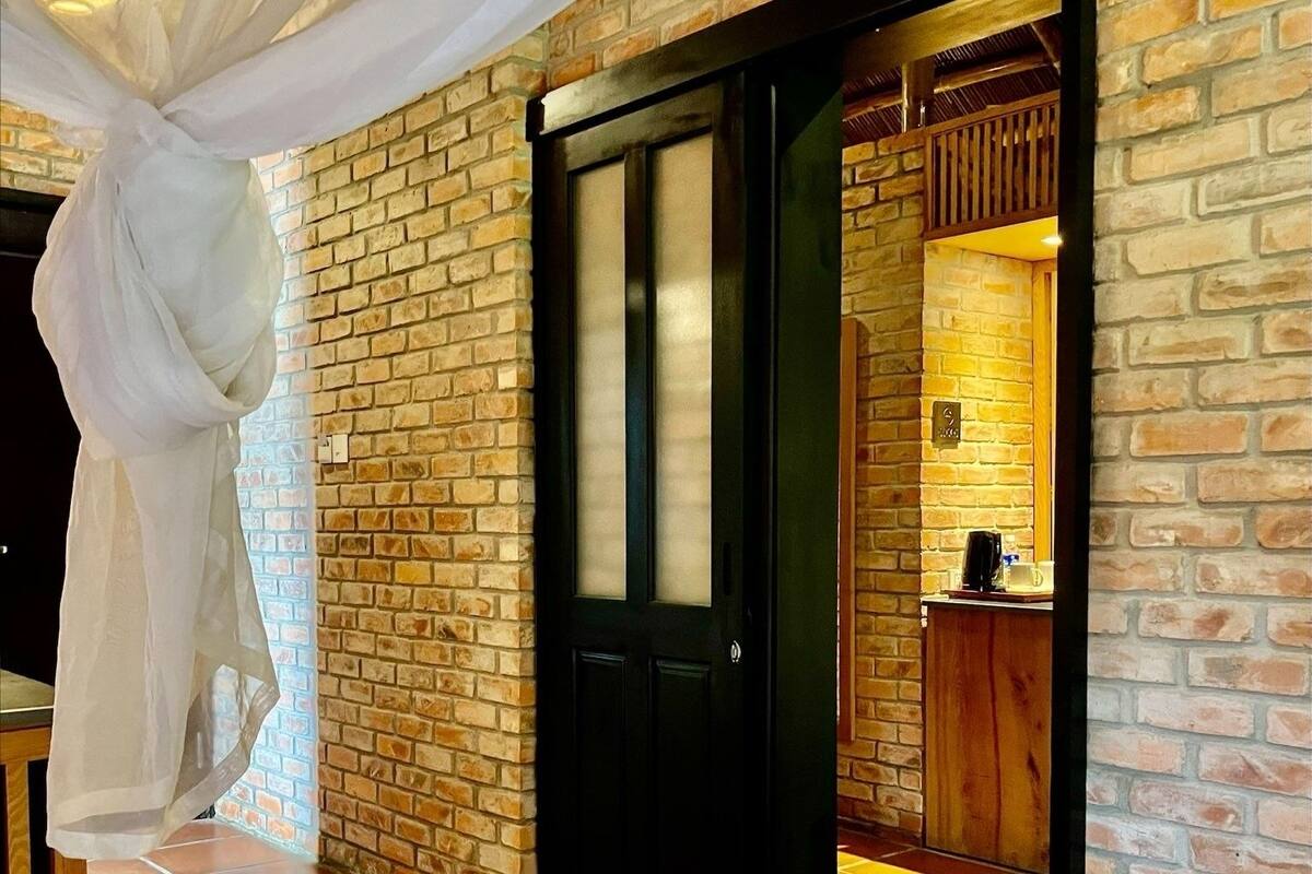 Une pièce avec un mur en briques, une porte noire et un lit blanc.