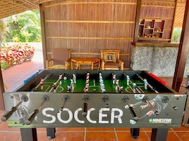 A foosball table labeled "SOCCER" with multiple players, set in a room with a bamboo wall and a small wooden table.