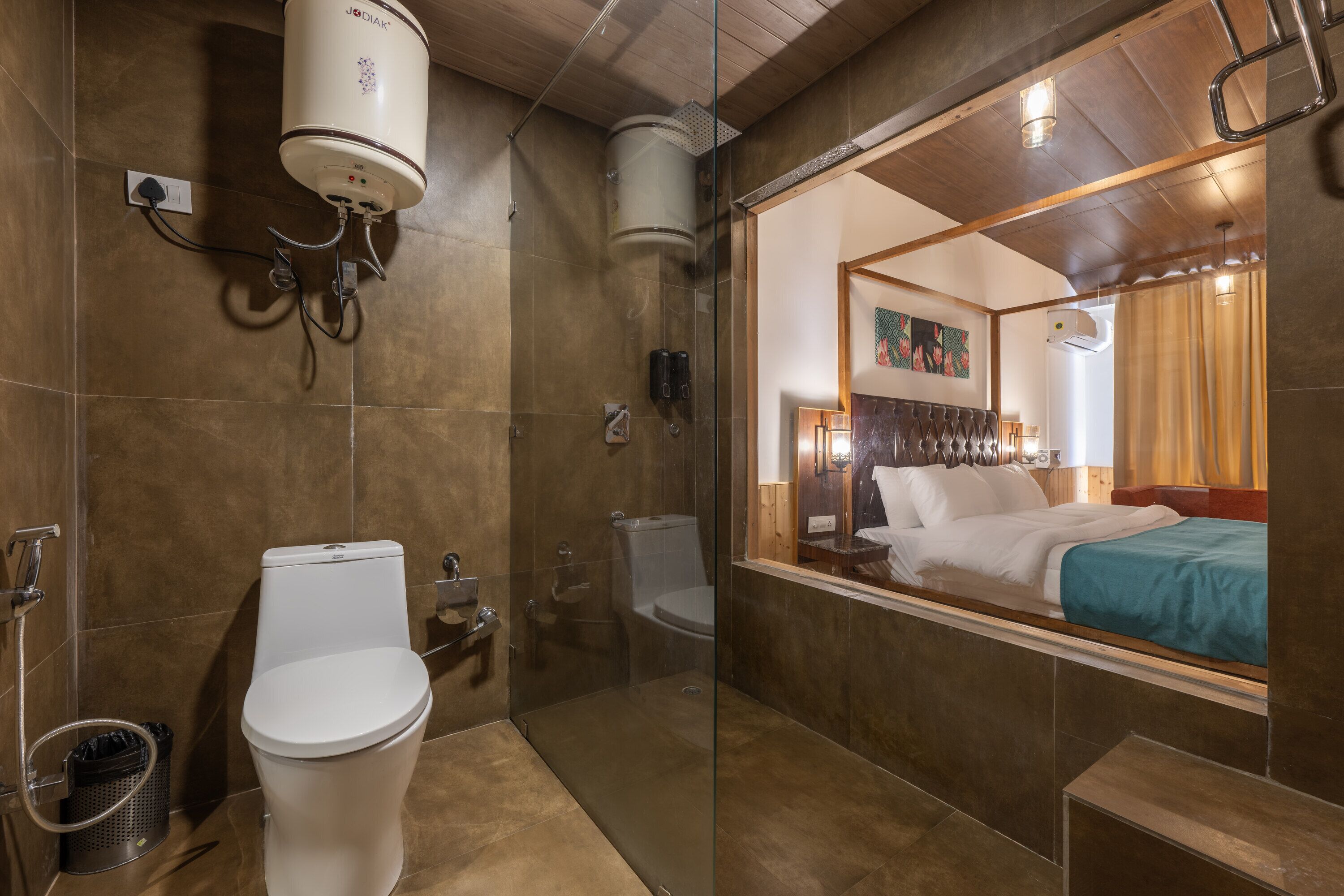 Un baño moderno con inodoro, bidé y ducha. Se aprecia un espejo grande que refleja una cama y una ventana con cortinas.
