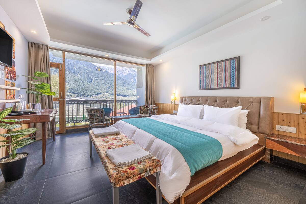 Habitación de hotel moderna con una cama grande, un escritorio y un balcón con vistas a la montaña.
