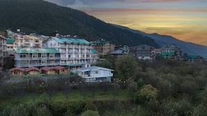 Un hotel de varios pisos con balcones, ubicado en una zona montañosa con abundante vegetación y colinas al fondo.