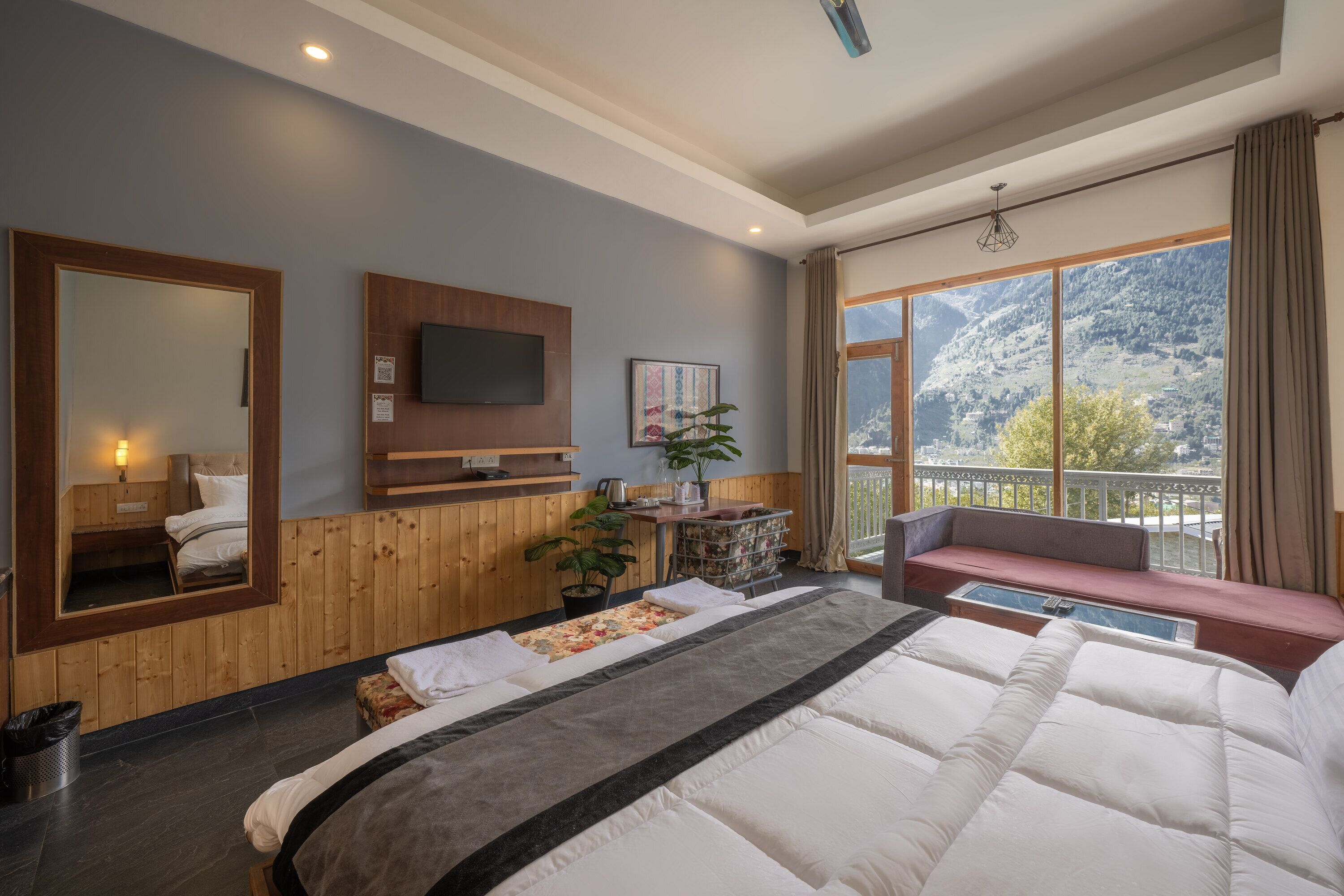Ein Hotelzimmer mit einem großen Bett, einem an der Wand befestigten Fernseher, einem Fenster mit Blick auf Berge und einem Balkon mit Sitzgelegenheit.