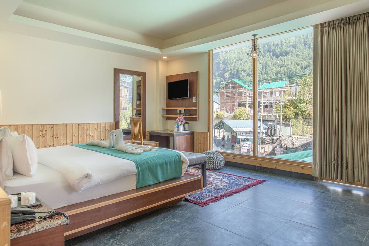Habitación de hotel con cama, televisor montado en la pared, ventana con vistas a un edificio y cabecero de madera.