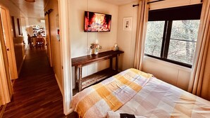 A bedroom with a bed, a TV, a window with curtains, a ceiling fan, and a hallway leading to a dining area. - The Hide, Rustic charm meets coastal calm. (Bouvard)