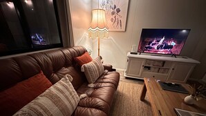 A living room with a brown leather sofa, a wooden coffee table, a TV on a white cabinet, and a floor lamp. - The Hide, Rustic charm meets coastal calm. (Bouvard)
