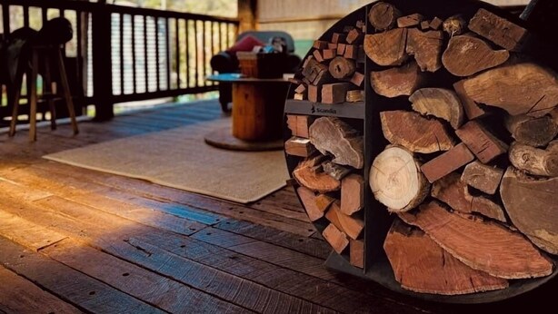 A covered outdoor area with a wooden deck, a fire pit with logs, and a table with chairs. - The Hide, Rustic charm meets coastal calm. (Bouvard)
