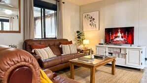 A living room with a leather sofa, a coffee table, a TV displaying a fireplace, and a cabinet with drawers. - The Hide, Rustic charm meets coastal calm. (Bouvard)