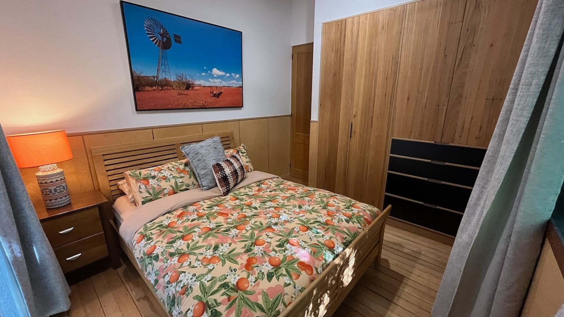 Ein Schlafzimmer mit einem Bett, einem Nachttisch, einer Lampe, einem hölzernen Kleiderschrank und einem Windmühlenbild.
