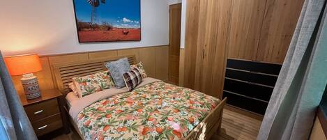 Ein Schlafzimmer mit einem Bett, einem Nachttisch, einer Lampe, einem hölzernen Kleiderschrank und einem Windmühlenbild.