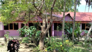 A building with a red roof and purple walls, surrounded by various plants and trees. - Havelock Harmony Resort (Port Blair)
