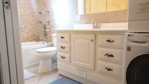 A bathroom with a bathtub, toilet, sink, and a washing machine. - The Secret In the Springs Hideaway, a luxury efficiency at the Legacy Trail (Sarasota)