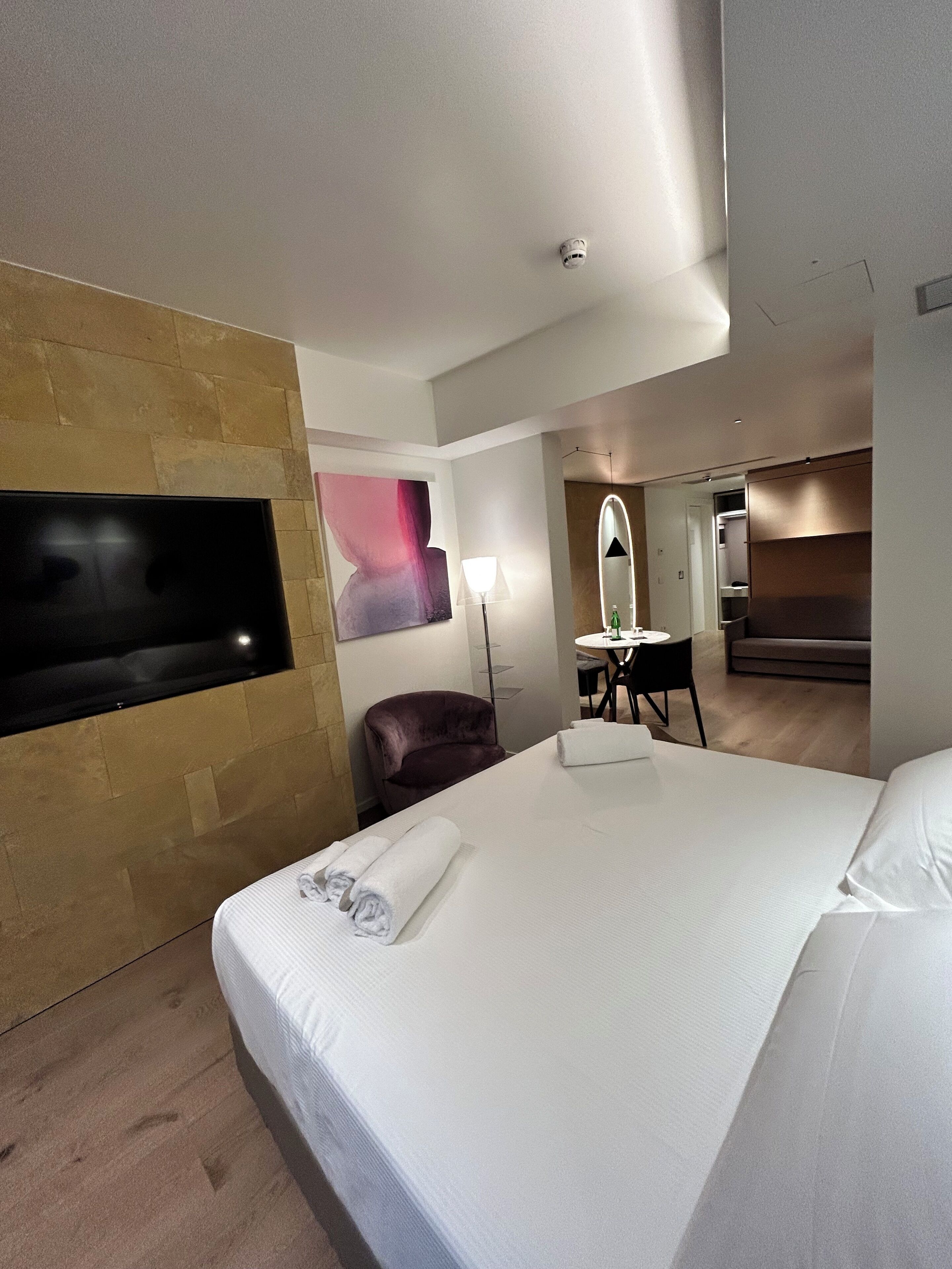 Habitación de hotel con una cama grande, un televisor de pantalla plana montado en la pared, un escritorio con una silla, un espejo y una pared de acento de madera.