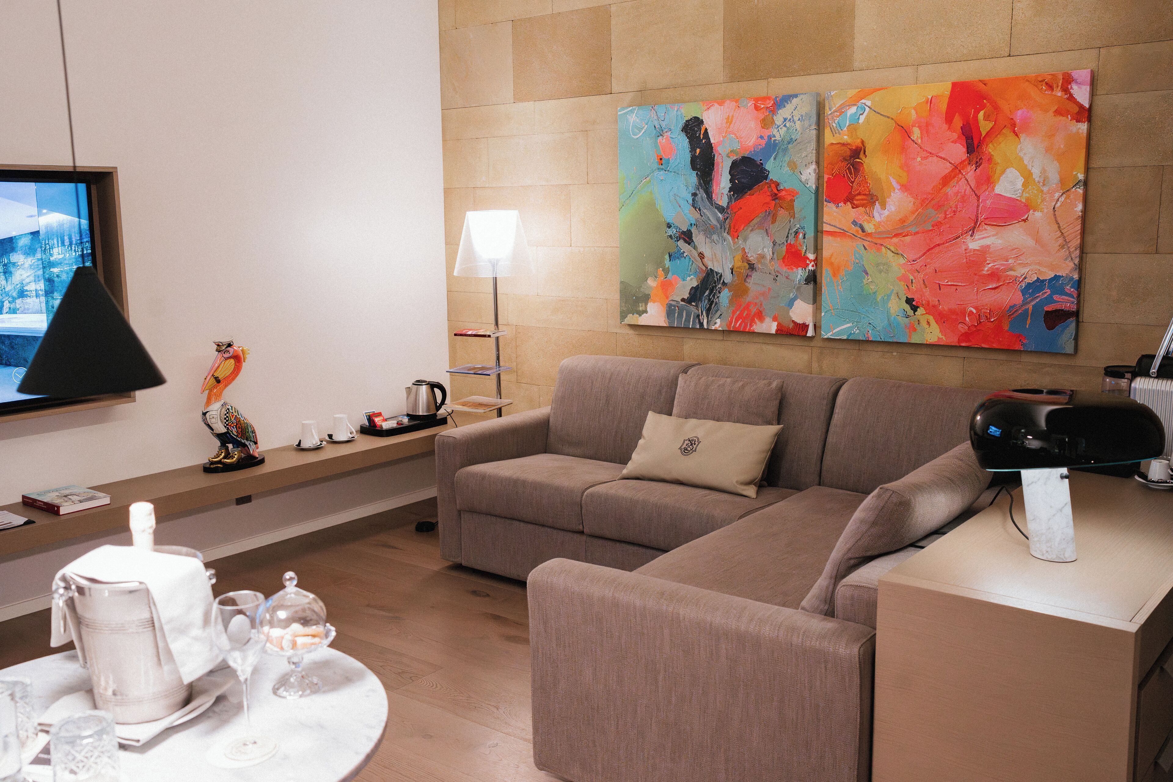 Ein modernes Wohnzimmer mit einer Eckcouch, einem Flachbildfernseher, abstrakter Kunst an der Wand, einem Couchtisch mit einer Teekanne und einer Lampe.