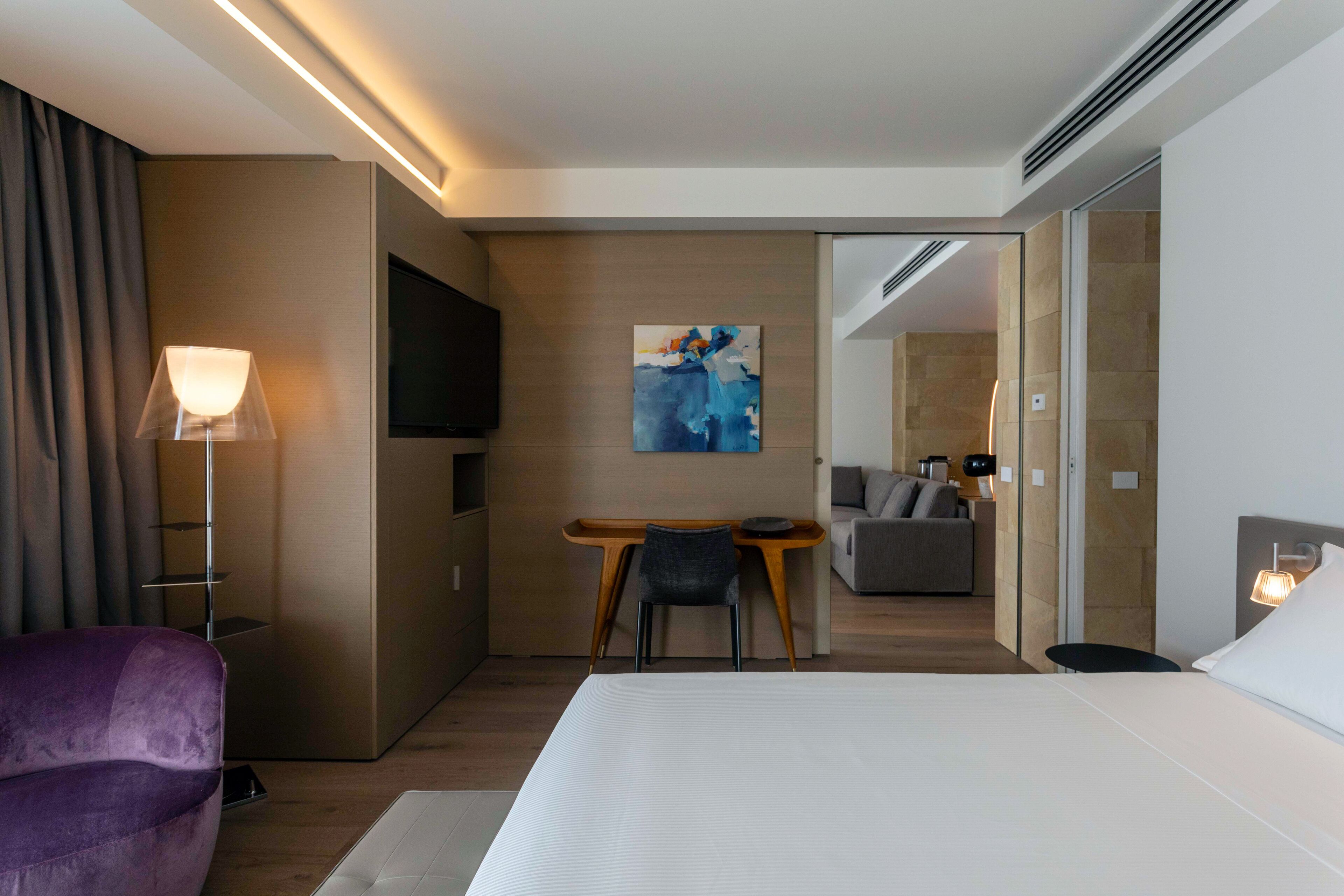 Una habitación de hotel moderna con una cama grande, un escritorio con una silla, un televisor y un cuadro en la pared.
