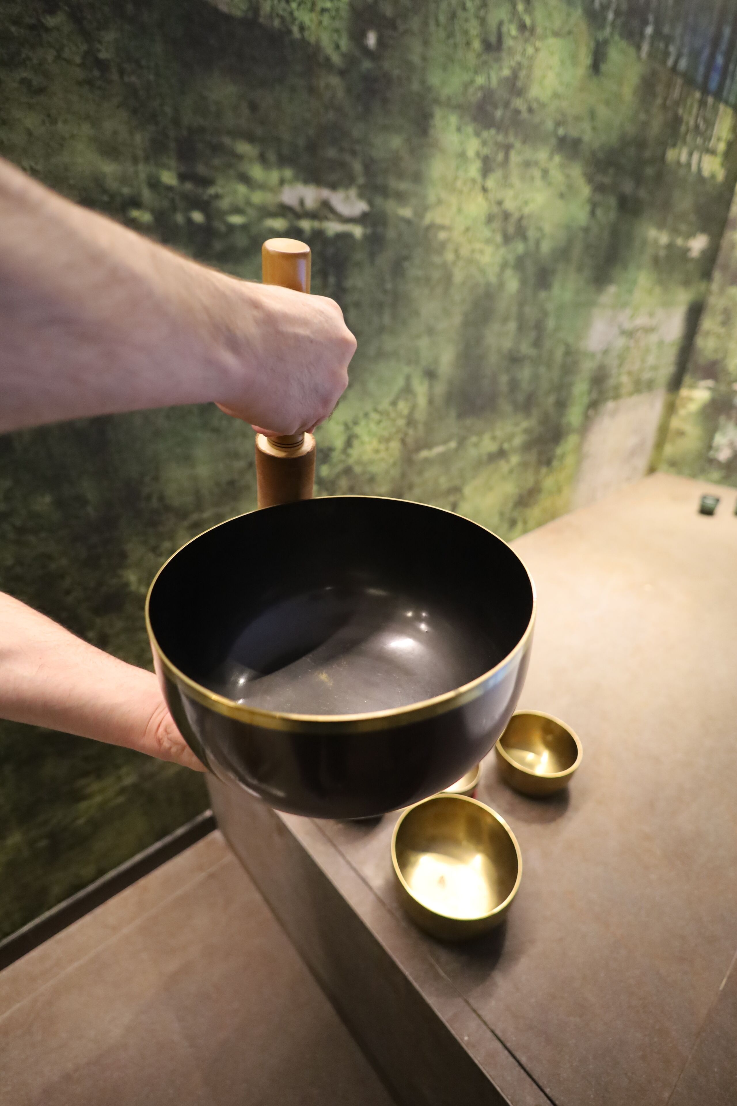 A hand holding a large black bowl with a golden handle, placed on a counter with two smaller golden bowls beside it.