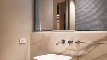 Un bagno moderno con un ampio lavabo in marmo, uno specchio sopra e una finestra con persiane.