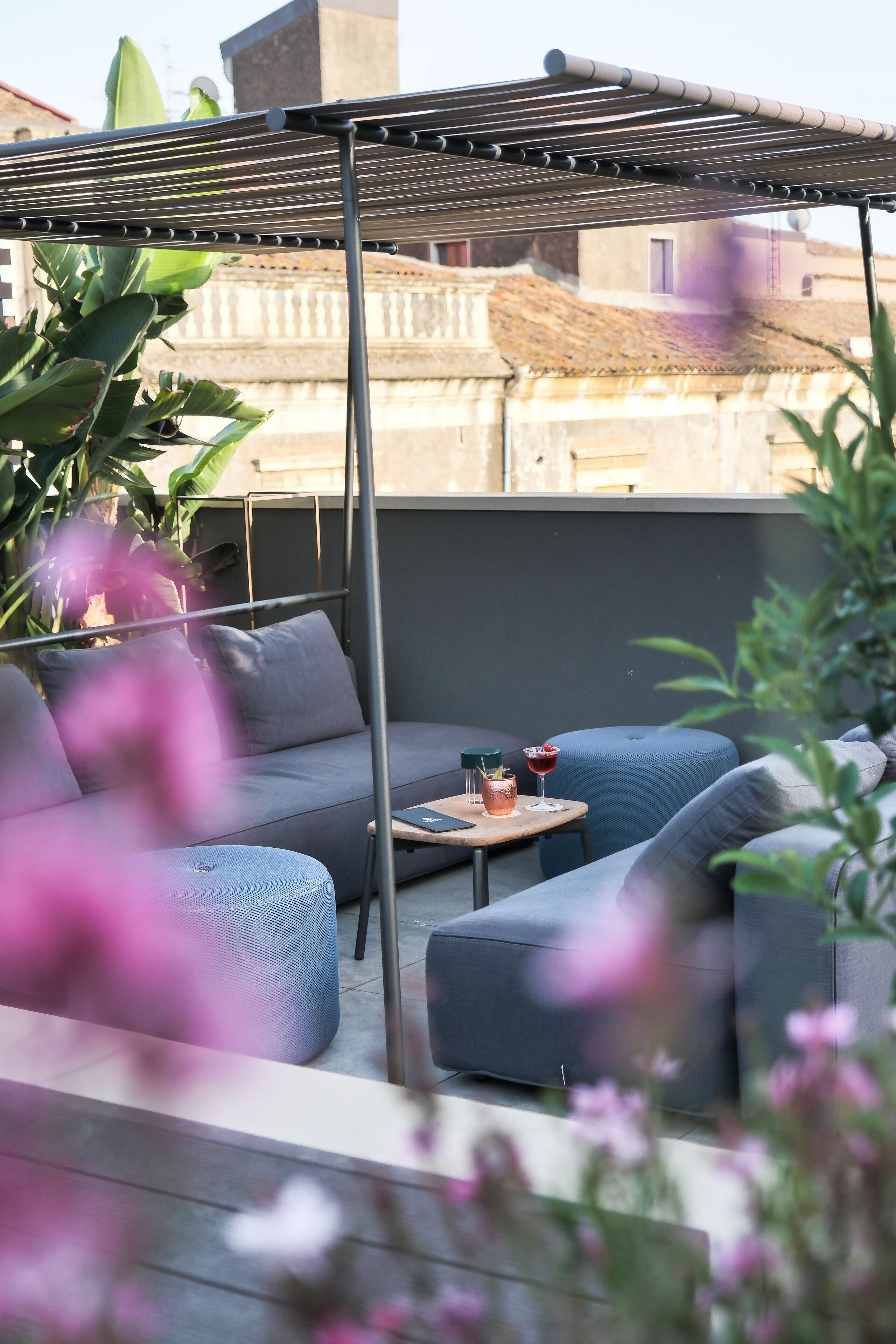 A rooftop patio with a pergola, seating area, and a table with drinks.