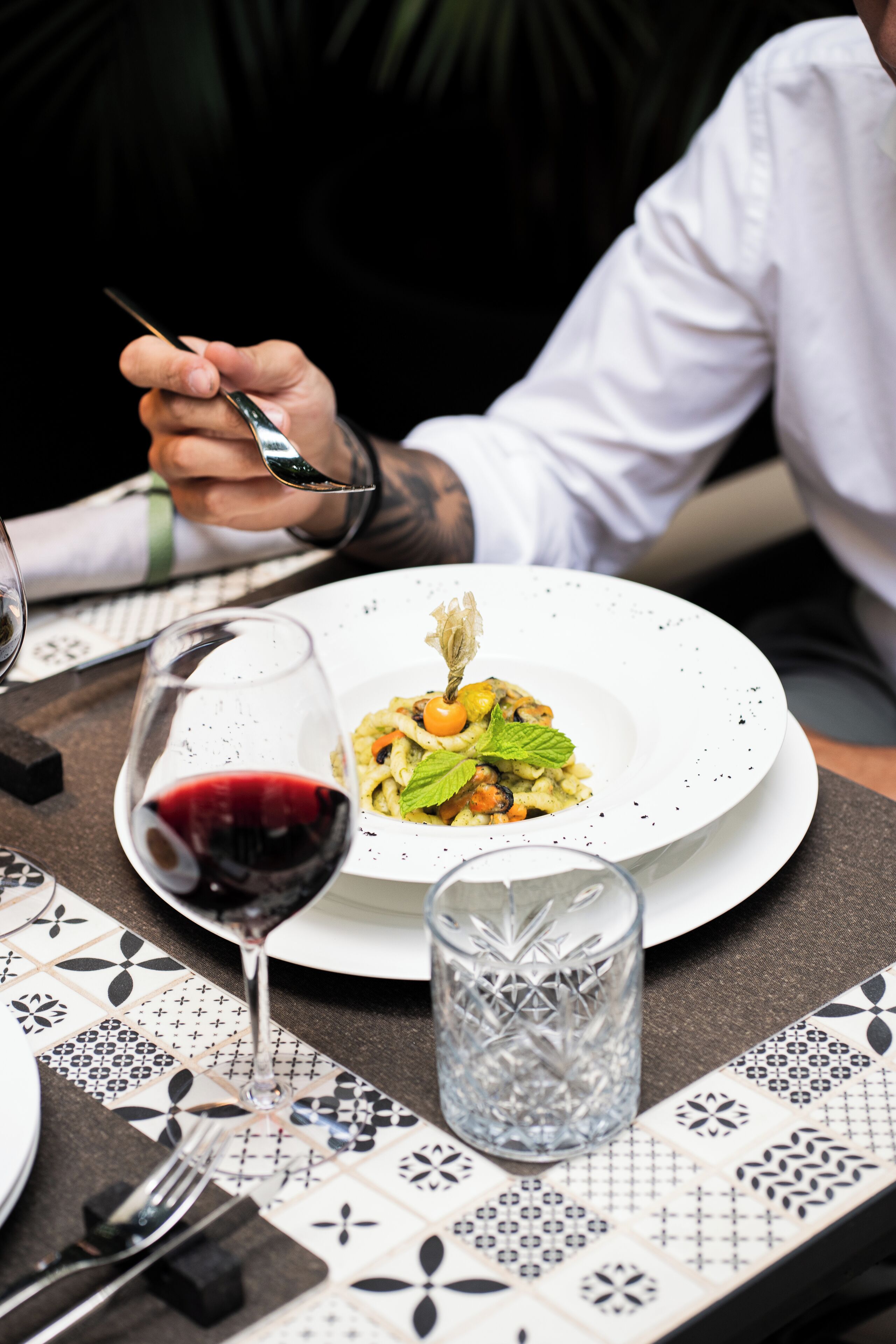 Una mesa con un plato de comida, una copa de vino tinto y un vaso transparente.