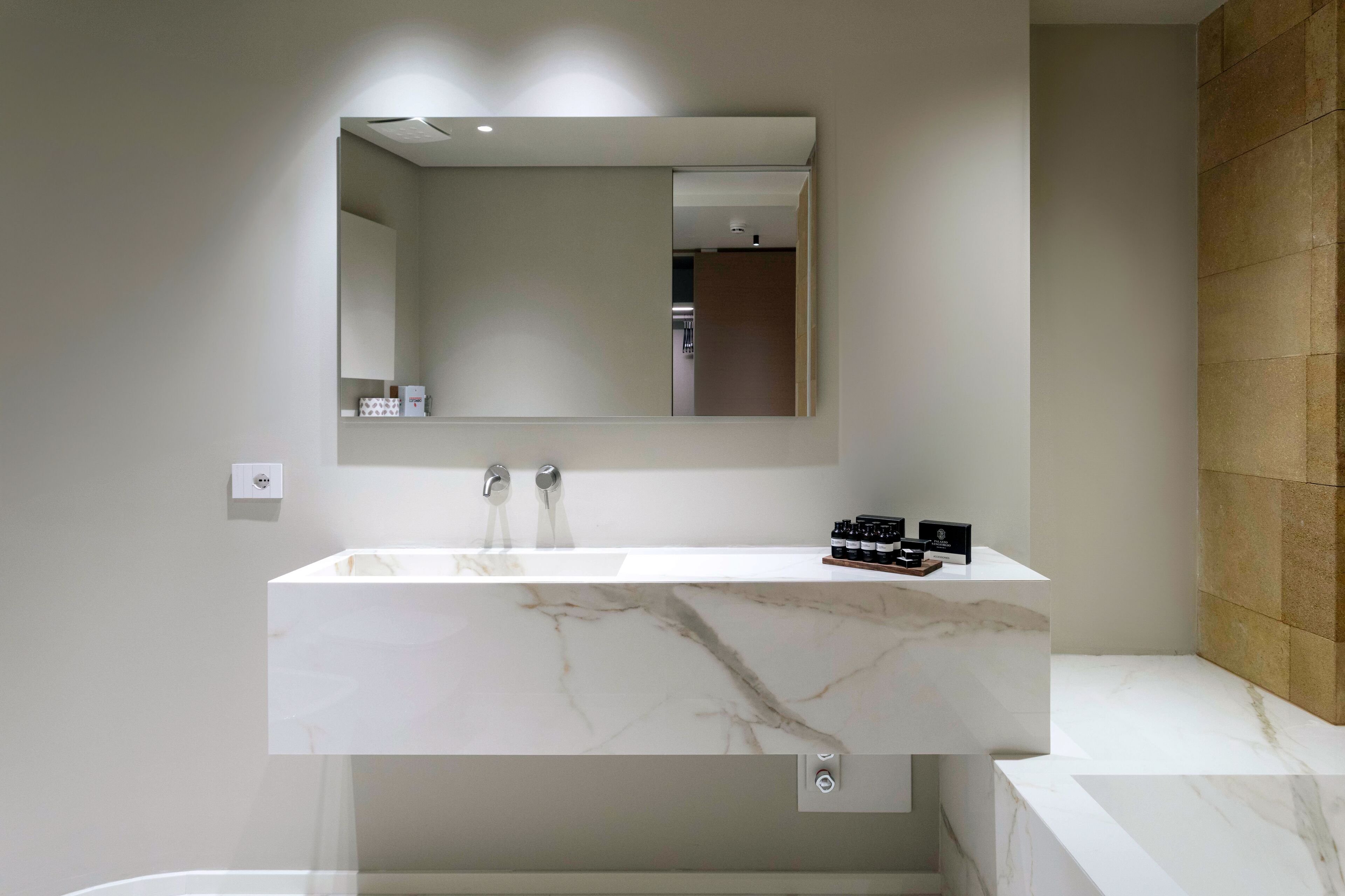A modern bathroom with a marble sink, a large mirror, and a wooden accent wall.