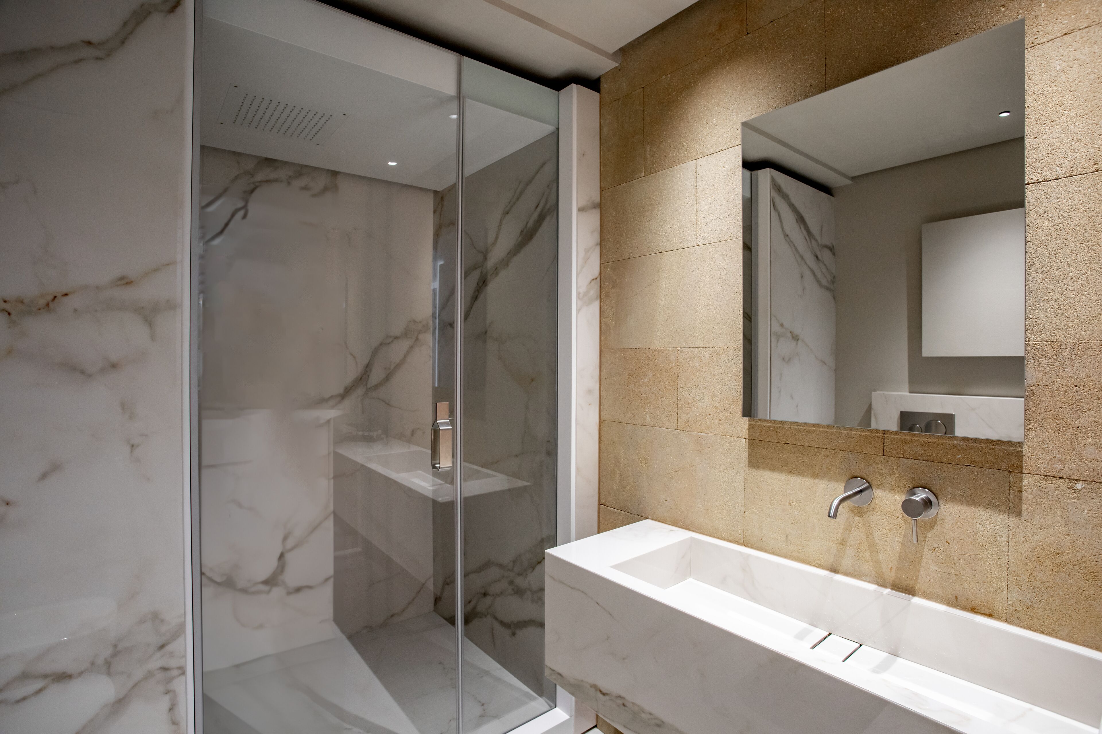 A modern bathroom with a glass-enclosed shower, a marble-tiled wall, and a large sink with a mirror above it.