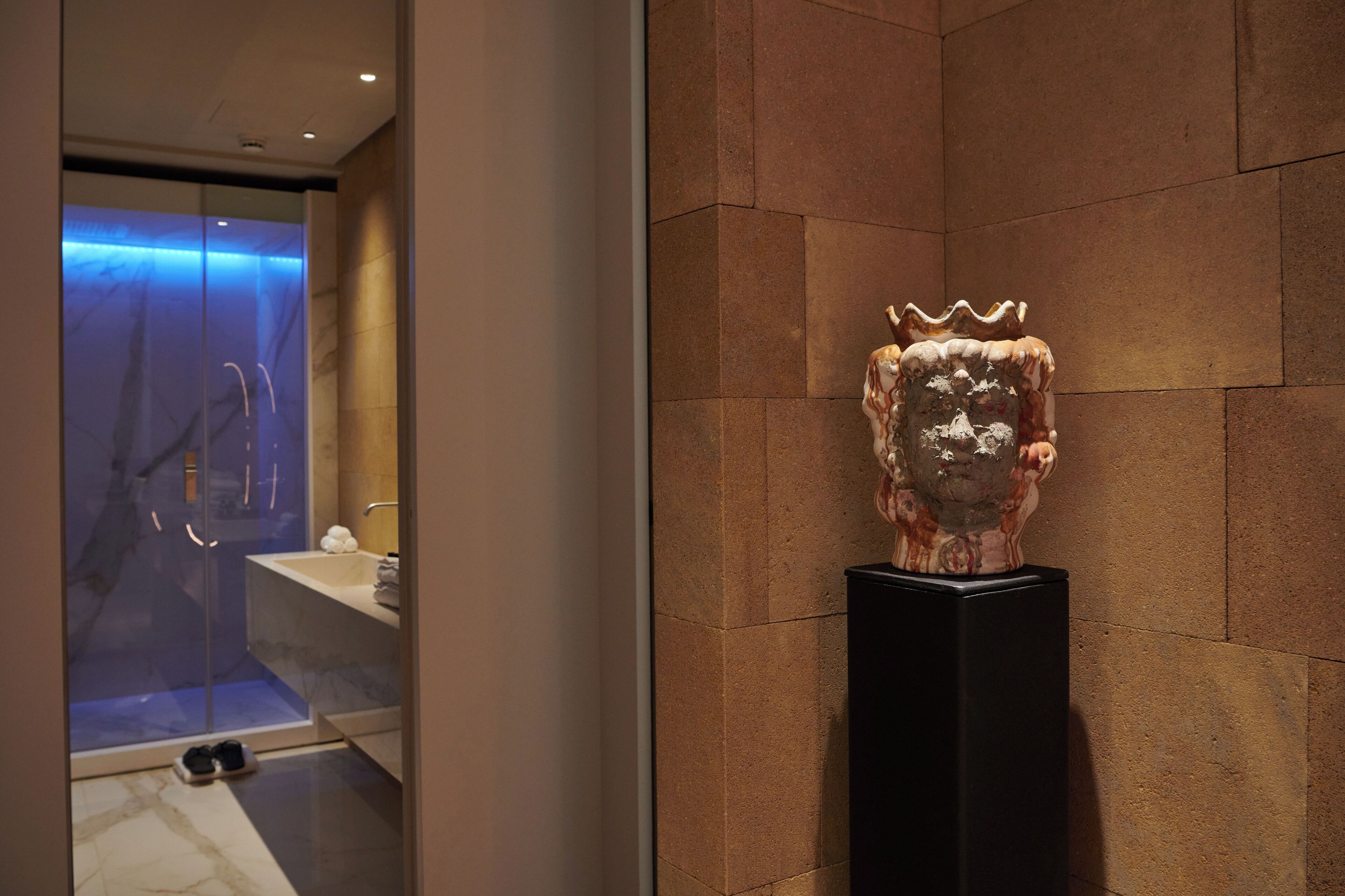 A bathroom with a marble floor, a glass shower enclosure, and a decorative sculpture on a pedestal.