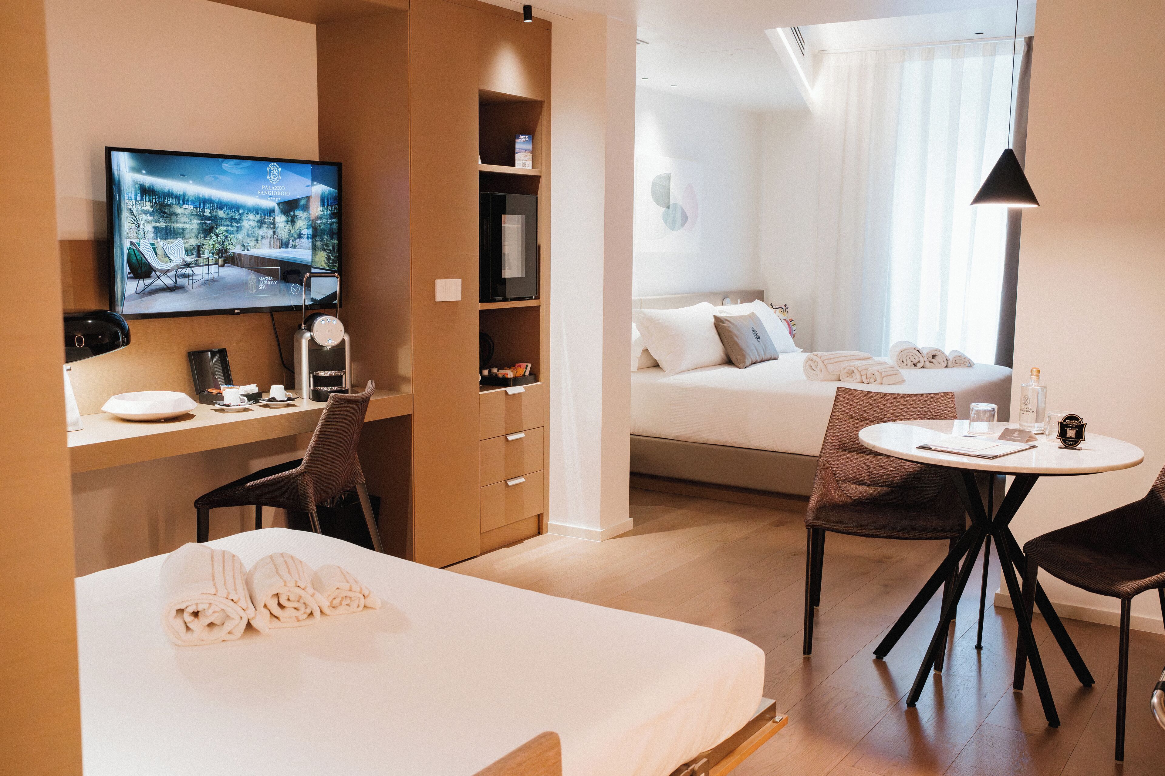 A hotel room with a bed, a desk with a computer, a TV, a dining table with chairs, and a sofa.