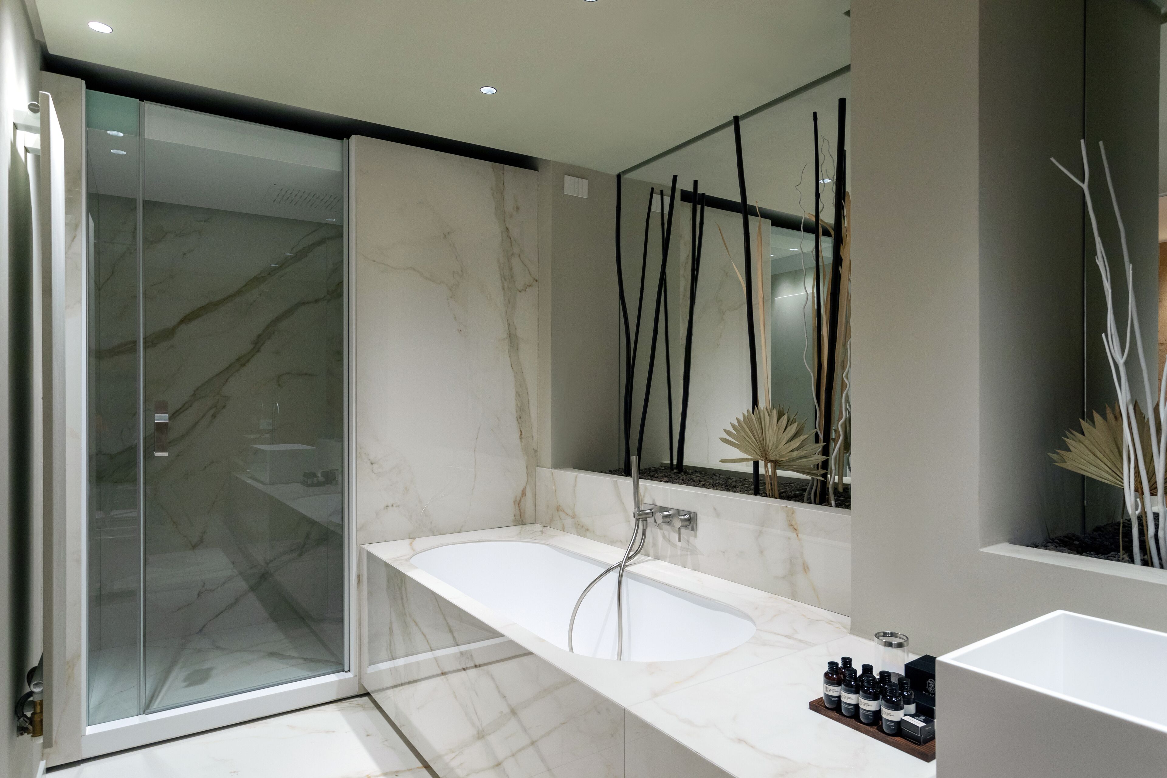 Un bagno moderno con cabina doccia in vetro, una vasca da bagno in marmo e un mobile lavabo con articoli da toilette.