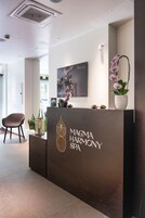 A reception desk with a logo for Magma Harmony Spa, a framed picture on the wall, and a potted orchid.