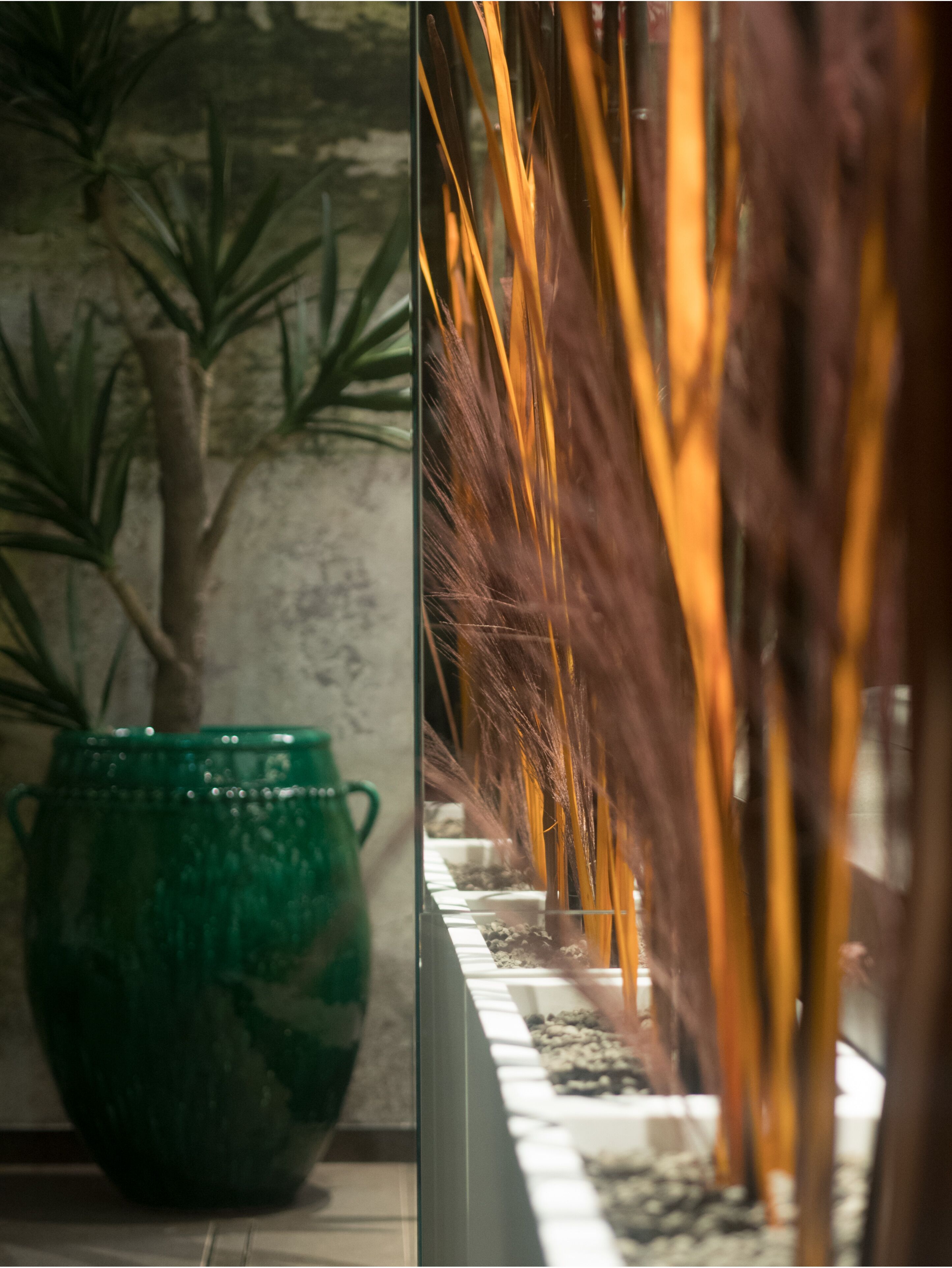 A green vase on a table, a plant, and a decorative arrangement with tall, thin, golden-brown elements.