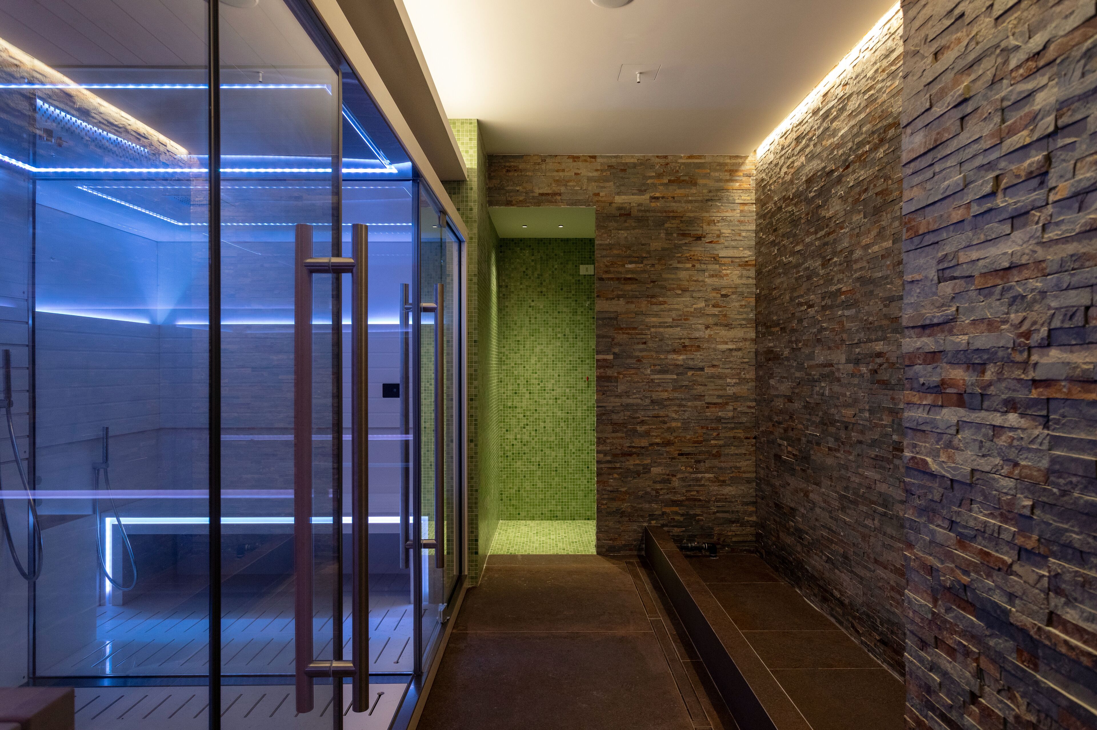 A modern bathroom with a glass shower enclosure, a stone wall, and a tiled floor.