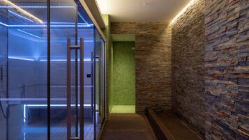 A modern bathroom with a glass shower enclosure, a stone wall, and a tiled floor.